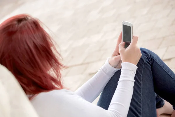 예쁜 미소 빨간 머리 여자 보내는 메시지 에 그녀의 휴대 전화 — 스톡 사진