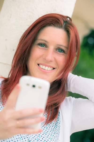 Cute smiling redheaded woman against an old wall with her mobile — Stock Photo, Image