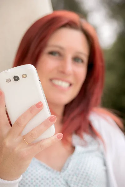 Linda mujer pelirroja sonriente contra una vieja pared con su teléfono móvil en la mano — Foto de Stock
