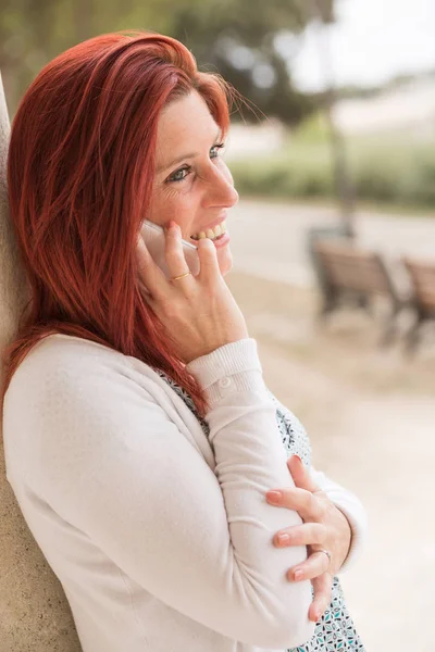 Linda mujer pelirroja sonriente haciendo una llamada con su teléfono celular — Foto de Stock