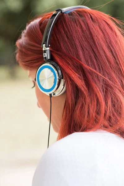 Redhead kvinna lyssnar på musik i hörlurar med grönska i t — Stockfoto