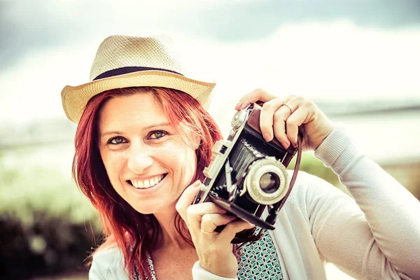 Eski bir kamera ile fotoğraf çekmek güzel gülümseyen kızıl saçlı kadının portresi. — Stok fotoğraf