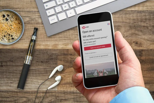 Человек в офисе использует свой смартфон, чтобы увидеть информацию о банковской компании HSBC. — стоковое фото