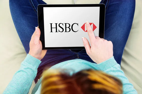 Woman sitting cross-legged on her couch and using her touch pad to see information about hsbc compagny — Stock Photo, Image
