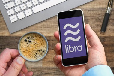 Terazi logosu ile elinde bir akıllı telefon tutan adam, facebook şirketi tarafından oluşturulan yeni kripto para birimi