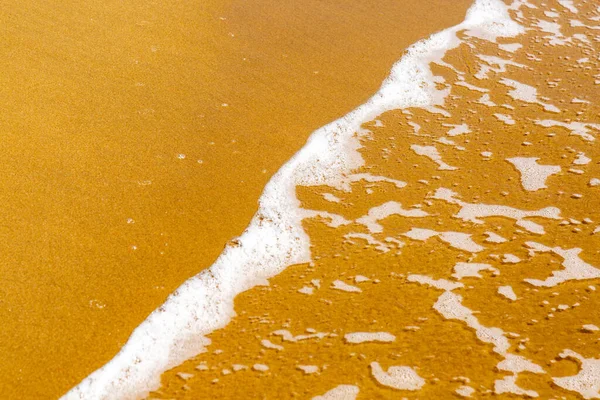 海の端に金色の砂で柔らかい波の泡を閉じ込めます — ストック写真
