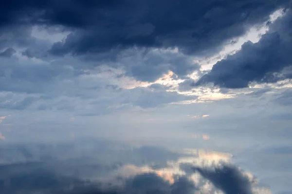 Gloomy clouds covered the sky over the ocean. The surface of the ocean is calm and reflects the clouds.