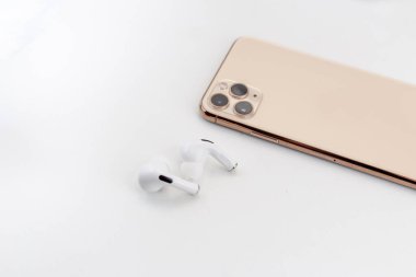 Bir cep telefonunun yanında beyaz kablosuz kulaklık.