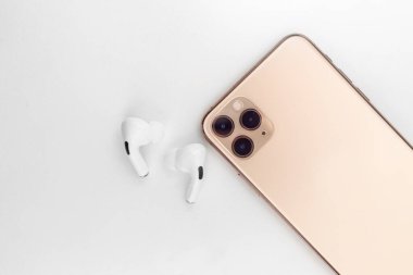 Bir cep telefonunun yanında beyaz kablosuz kulaklık.