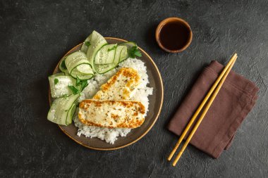 Pirinç ve salatalık salatası siyah arka plan, tofu biftek alanı kopyalayın. Kavrulmuş kızarmış tofu biftek ile sağlıklı vegan vejetaryen yemek yemek.