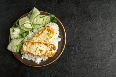 Pirinç ve salatalık salatası siyah arka plan, tofu biftek alanı kopyalayın. Kavrulmuş kızarmış tofu biftek ile sağlıklı vegan vejetaryen yemek yemek.