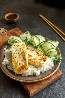 Pirinç ve salatalık salatası siyah arka plan, tofu biftek alanı kopyalayın. Kavrulmuş kızarmış tofu biftek ile sağlıklı vegan vejetaryen yemek yemek.