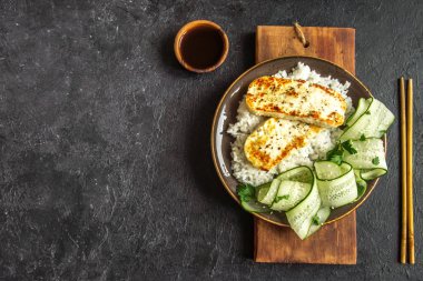 Pirinç ve salatalık salatası siyah arka plan, tofu biftek alanı kopyalayın. Kavrulmuş kızarmış tofu biftek ile sağlıklı vegan vejetaryen yemek yemek.