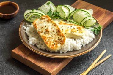 Pirinç ve salatalık salatası siyah arka plan, tofu biftek alanı kopyalayın. Kavrulmuş kızarmış tofu biftek ile sağlıklı vegan vejetaryen yemek yemek.