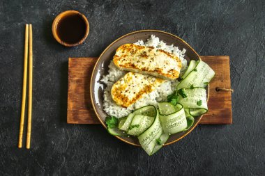 Pirinç ve salatalık salatası siyah arka plan, tofu biftek alanı kopyalayın. Kavrulmuş kızarmış tofu biftek ile sağlıklı vegan vejetaryen yemek yemek.