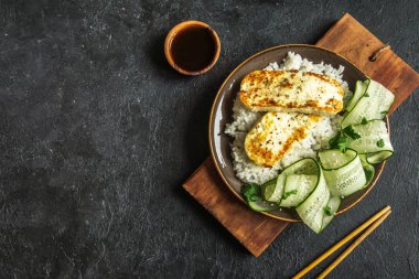 Pirinç ve salatalık salatası siyah arka plan, tofu biftek alanı kopyalayın. Kavrulmuş kızarmış tofu biftek ile sağlıklı vegan vejetaryen yemek yemek.