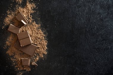 Kırık siyah çikolata parçaları ve kakao tozu. Çikolata onr koyu taş arka plan topakları.