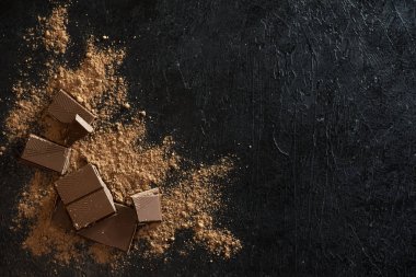 Kırık siyah çikolata parçaları ve kakao tozu. Çikolata onr koyu taş arka plan topakları.