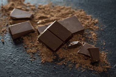 Kırık siyah çikolata parçaları ve kakao tozu. Çikolata onr koyu taş arka plan topakları.