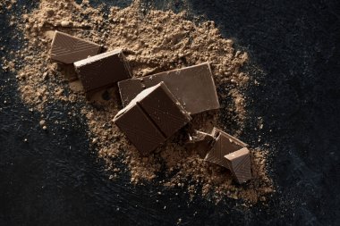 Kırık siyah çikolata parçaları ve kakao tozu. Çikolata onr koyu taş arka plan topakları.