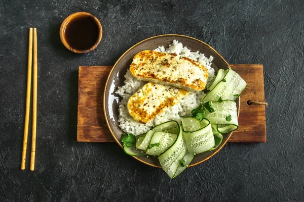 Pirinç ve salatalık salatası siyah arka plan, tofu biftek alanı kopyalayın. Kavrulmuş kızarmış tofu biftek ile sağlıklı vegan vejetaryen yemek yemek.