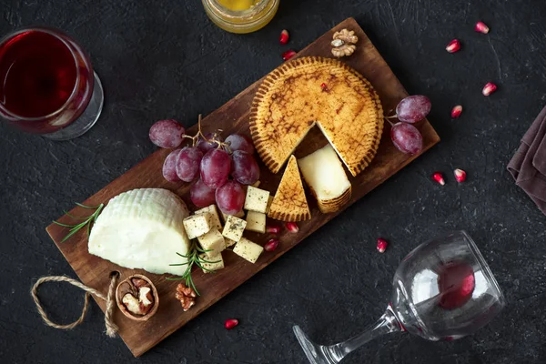 Cheese platter with assorted cheeses, grapes, nuts over black background, copy space. Italian cheese and fruit platter with honey and wine.