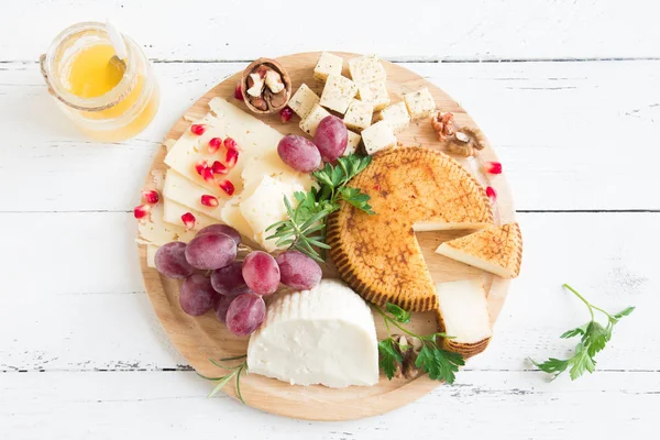 Cheese platter with assorted cheeses, grapes, nuts and honey over white wooden background, copy space. Italian cheese and fruit platter.