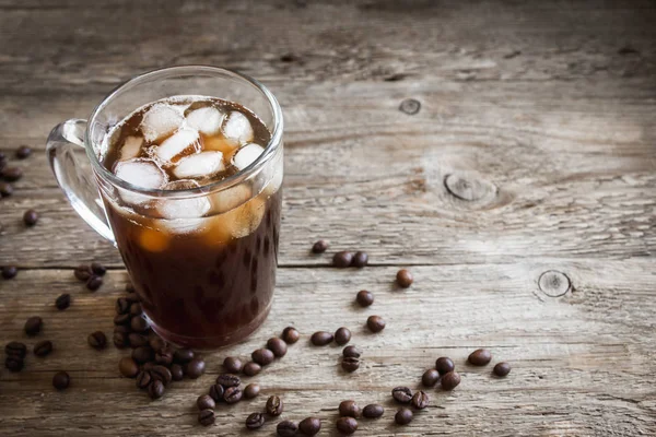 Iced coffee and coffee beans over rustic wooden table, copy space. Iced black coffee for refreshing.