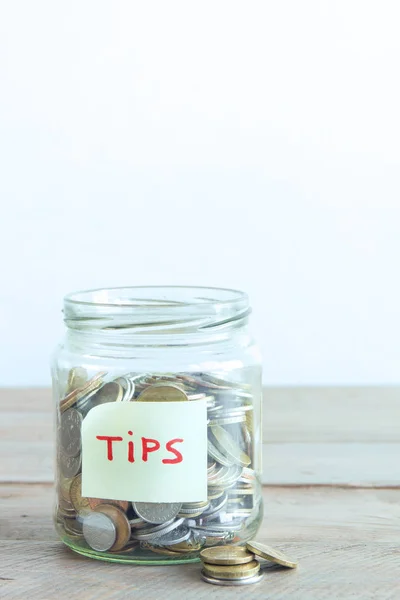 Coins in glass jar with Tips label. Money savings, tips and donation concept, copy space.