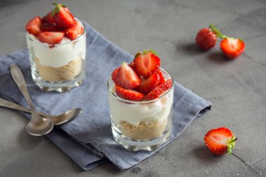 Çilekli pasta ister taze çilek ve gri beton zemin üzerine krem peynir ile bardaklarda mini tatlı. Sağlıklı ev yapımı potrion tatlı.