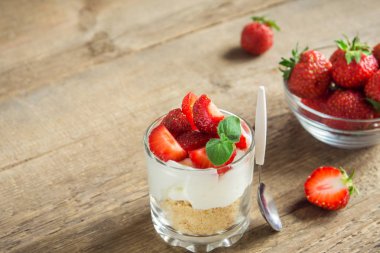 Bardakta çilekli cheesecake ve ahşap zemin üzerinde taze çilek ve krem peynir. Sağlıklı ev yapımı tatlı..