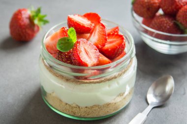 Çilekli cheesecake taze çilek ve gri beton zemin üzerine krem peynir ile cam kavanoza. Sağlıklı ev yapımı organik tatlı.