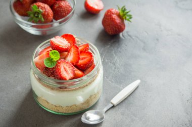Çilekli cheesecake taze çilek ve gri beton zemin üzerine krem peynir ile cam kavanoza. Sağlıklı ev yapımı organik tatlı.