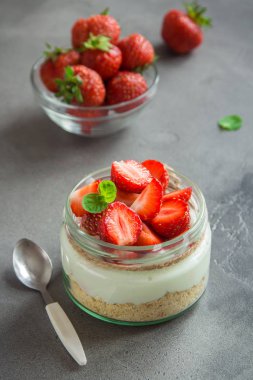 Çilekli cheesecake taze çilek ve gri beton zemin üzerine krem peynir ile cam kavanoza. Sağlıklı ev yapımı tatlı.