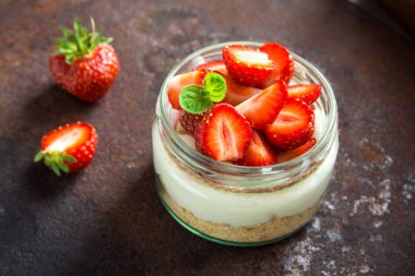 Çilekli cheesecake taze çilek ve krem peynir koyu arka plan üzerinde cam kavanoza. Sağlıklı ev yapımı tatlı.