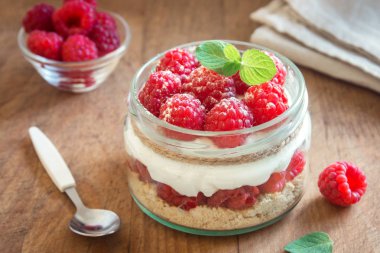 Ahududu cheesecake taze ahududu ve ahşap zemin üzerine krem peynir ile cam kavanoza. Sağlıklı ev yapımı yaz katmanlı berry tatlı.