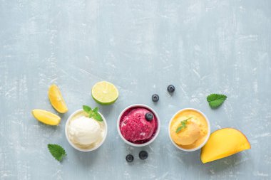 Üç çeşitli meyve ve çilek dondurma mavi arka plan, kopya alanı üzerinde. Dondurulmuş yoğurt veya dondurma ile limon, mango, yaban mersini - sağlıklı yaz tatlı.