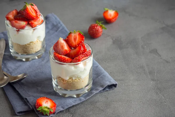 Strawberry trifle mini dessert in glasses with fresh strawberries and cream cheese  on grey concrete background. Healthy homemade potrion dessert.
