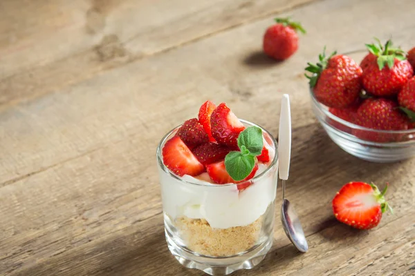 Bardakta çilekli cheesecake ve ahşap zemin üzerinde taze çilek ve krem peynir. Sağlıklı ev yapımı tatlı..
