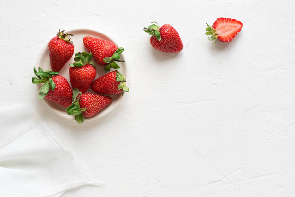 Fresh organic strawberries on plate on white concrete background, copy space, top view.