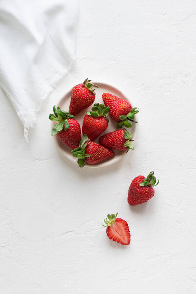 Fresh organic strawberries on plate on white concrete background, copy space, top view.