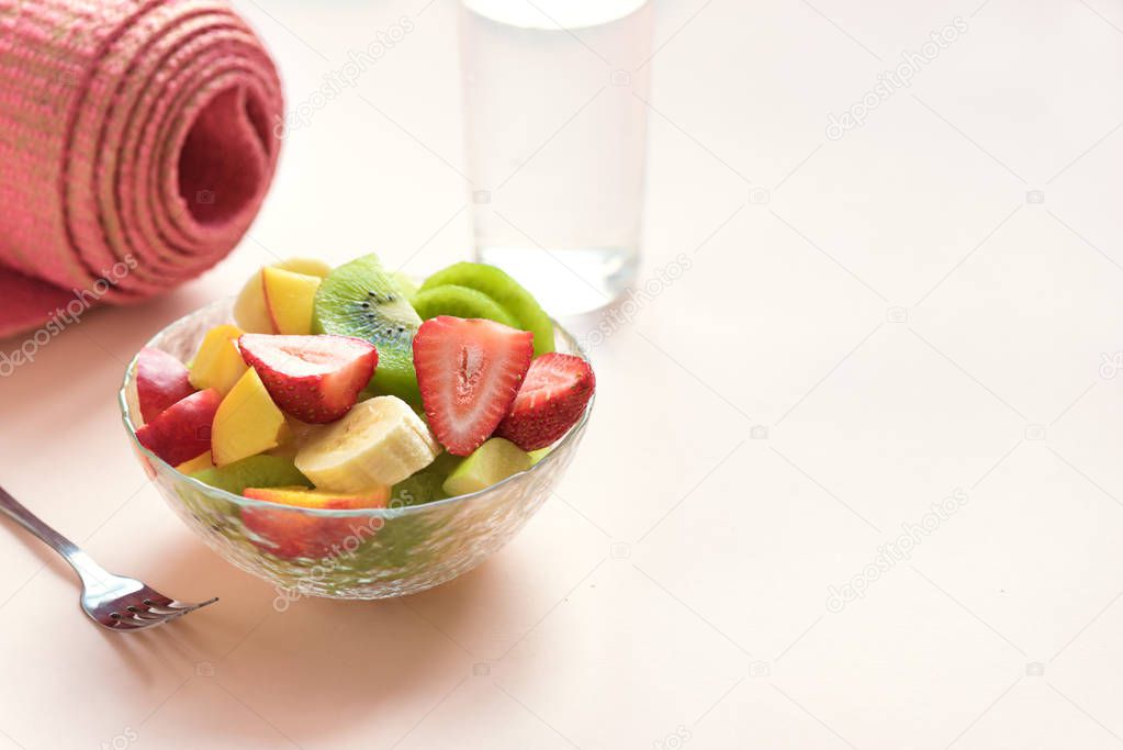 Sport and healthy lifestyle concept. Pink yoga mat and Fruit and Berries Salad in bowl for snack or breakfast on pink pastel background, copy space.