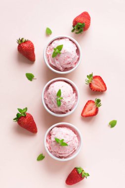 Çilekli dondurma ve taze çilek düz pastel pembe yatıyordu. Üç kâse çilekli dondurma, sağlıklı tatlı yaz.