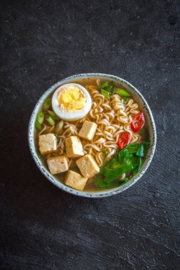 Japon ramen çorba tofu ve karanlık taş zemin üzerine yumurta ile. Ramen noodle ve tofu seramik kase, Asya geleneksel yemekleri ile miso çorbası.