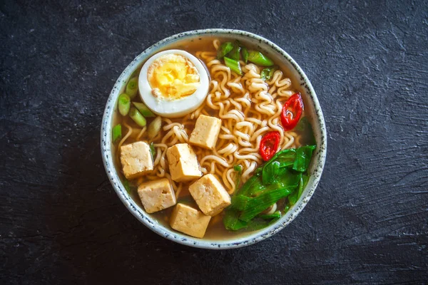 Japon ramen çorba tofu ve karanlık taş zemin üzerine yumurta ile. Ramen noodle ve tofu seramik kase, Asya geleneksel yemekleri ile miso çorbası.