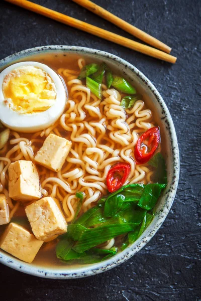 Japon ramen çorba tofu ve karanlık taş zemin üzerine yumurta ile. Ramen noodle ve tofu seramik kase, Asya geleneksel yemekleri ile miso çorbası.