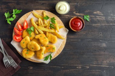 Tavuk nuggets, patates kızartması ve koyu ahşap arka plan, sosu alanı kopyalayın. Fried nuggets ve ketçap ve mayonez ile patates.