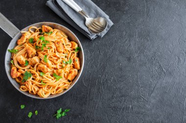 Domates soslu tavuk, maydanoz tavada spagetti makarna. Tavuk spagetti makarna kopya alanı, İtalyan yemeği siyah taş zemin üzerine.