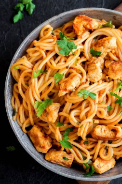 Domates soslu tavuk, maydanoz tavada spagetti makarna. Tavuk spagetti makarna kopya alanı, İtalyan yemeği siyah taş zemin üzerine.