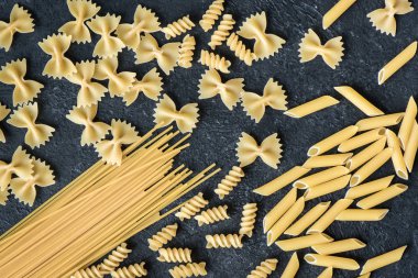 Siyah arka plan üzerine çeşitli pişmemiş çiğ makarna. İtalyan makarna: penne, farfalle, spagetti, düdük.